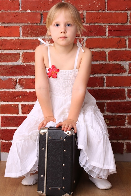 Beautiful little girl sitting on a suitcase. Travel ballet dancer
