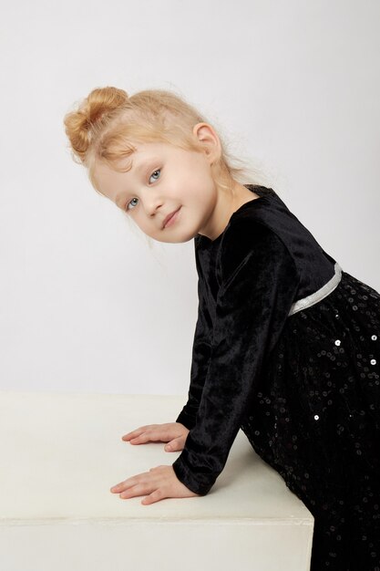 Beautiful little girl smiles, child in autumn clothes poses on a white wall