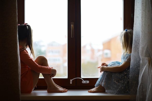 Beautiful little girl smiling and watching out the window A child looks out the window Young girl looking from window