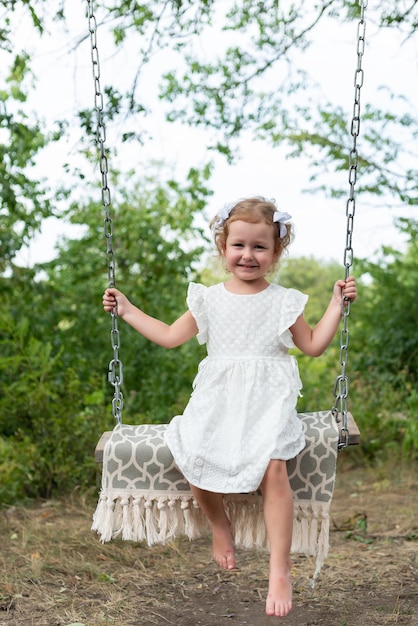 Beautiful little girl spends time outdoors Rides on a swing smiles and looks at the camera