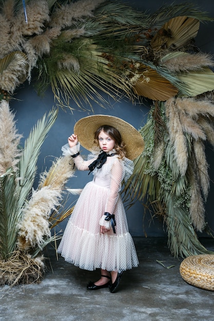 A beautiful little girl stands in a dress and a straw hat