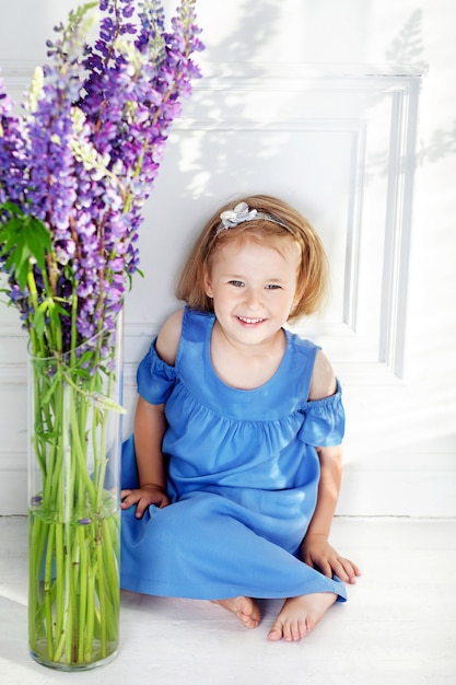 Beautiful little girl stands among violet flowers. A flower decor in an interior