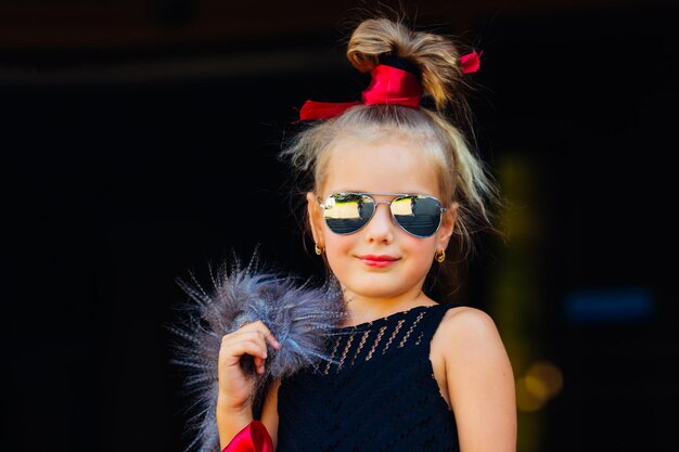 Beautiful little girl in sunglasses in a fur vest on a city street