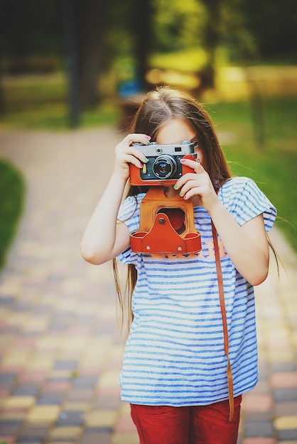 美しい少女は、日当たりの良い緑の森でビンテージカメラで写真を撮る