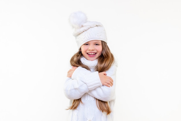 A beautiful little girl in a warm sweater and a winter hat is smiling. Warm children's clothing.