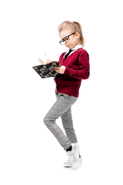 Beautiful little girl in white shirt and gray pants standing near white wall and posing like model