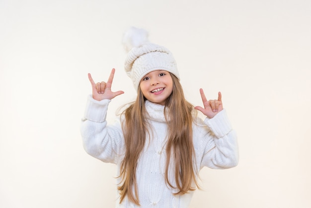 A beautiful little girl in a winter hat and sweater on a white isolated background is very happy and points her fingers to the side