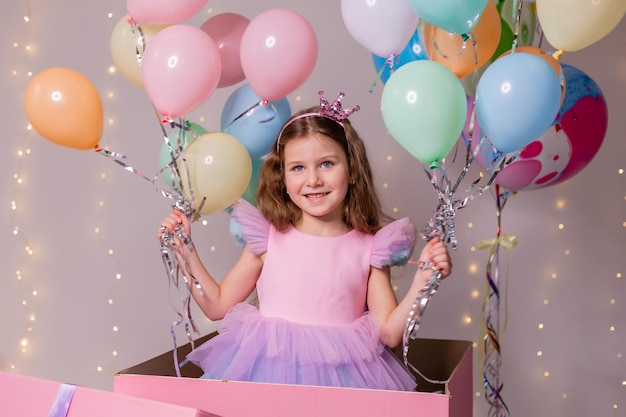 Beautiful little girl with balloons jumps out of a huge pink box child celebrates his birthday