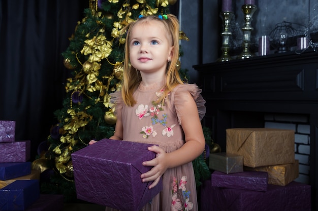 Beautiful little girl with blue eyes opens gift from Santa Claus near the Christmas tree