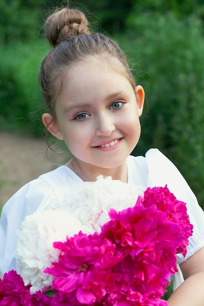 Una bellissima bambina con un mazzo di peonie in mano in un campo estivo servizio fotografico nel giardino primaverile sotto il cielo aperto