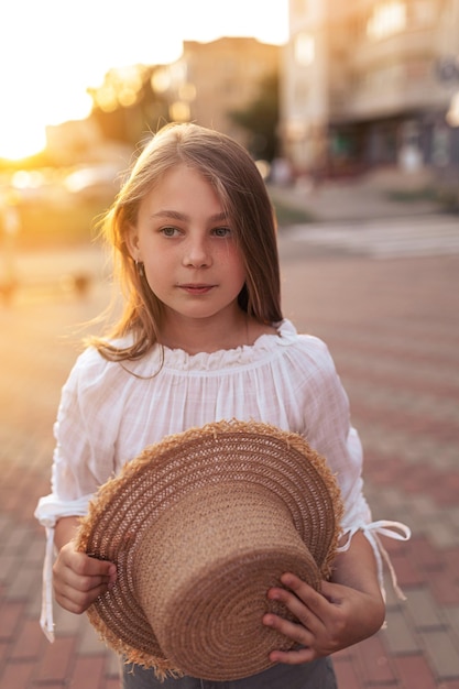 彼女の顔にそばかすのある美しい少女彼女は麦わら帽子をかぶって日没にいます