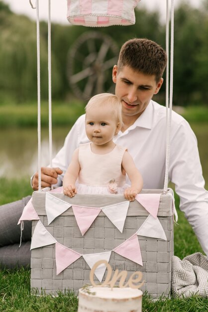 A beautiful little girl with her dad in a basket with a balloon and a cake celebrates her first birthday