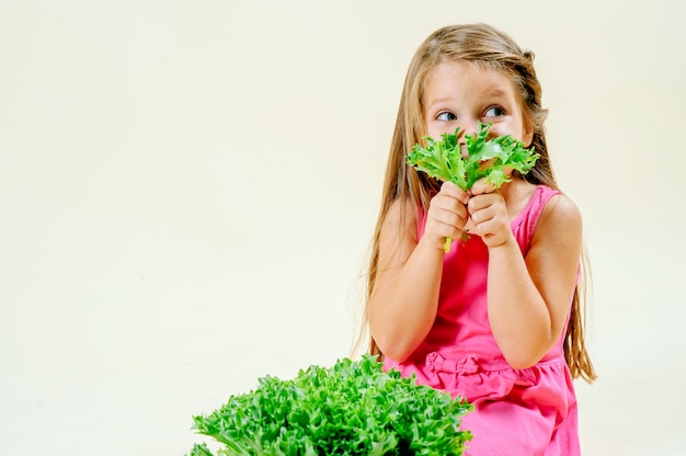 Beautiful little girl with lettuce in hand on a light monophonic background, proper nutrition