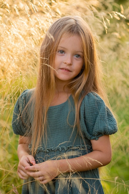 beautiful little girl with long blonde hair walks in a summer field at sunset