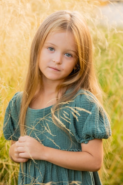 Photo beautiful little girl with long blonde hair walks in a summer field at sunset