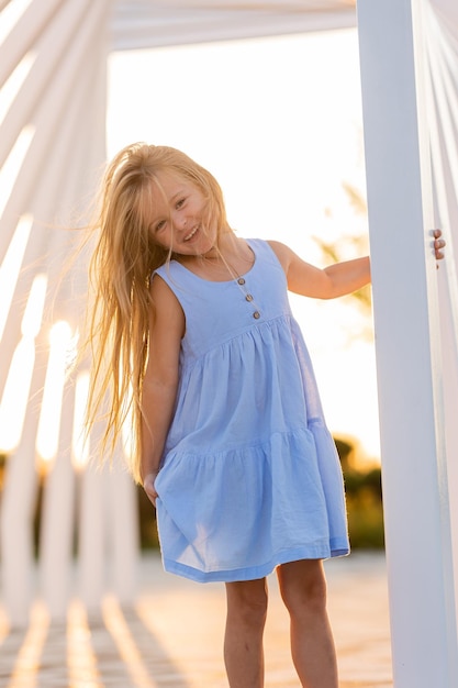 긴 금발 머리카락을 가진 아름다운 작은 소녀가 여름에 도시 공원에서 해가 지는 동안 고 있습니다.