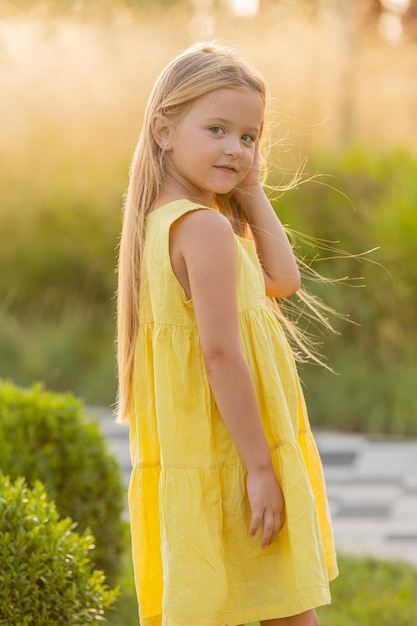 beautiful little girl with long blonde hair walks at sunset in the city park in summer