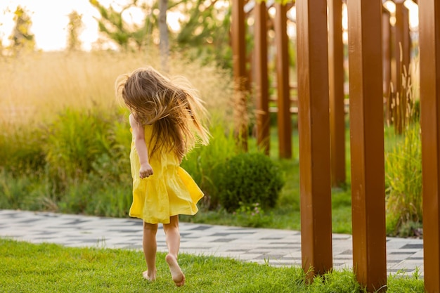 beautiful little girl with long blonde hair walks at sunset in the city park in summer