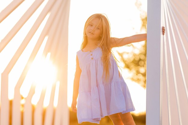 beautiful little girl with long brown hair walks at sunset in the city park in summer