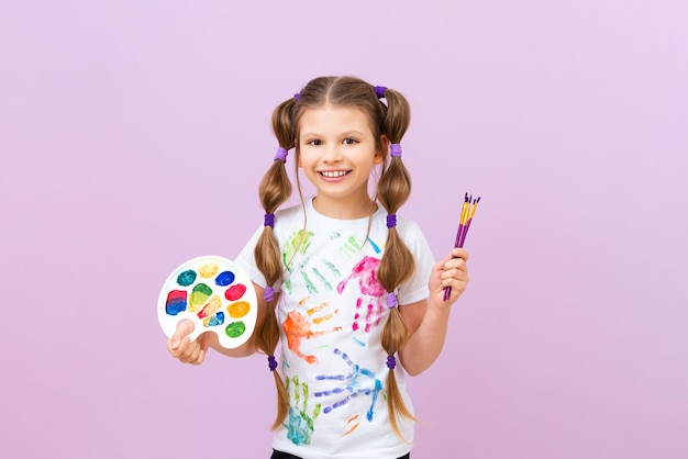 A beautiful little girl with paints and a palette in her hands the concept of painting pictures children's creativity and drawing