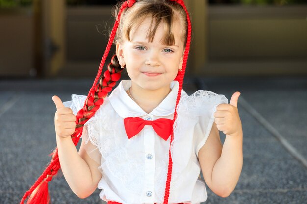 Beautiful little girl with red pigtails and bow tie. the child shows thumbs up. High quality photo