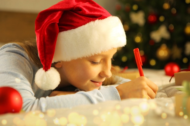 Beautiful little girl writing a letter to santa claus in the christmas interior