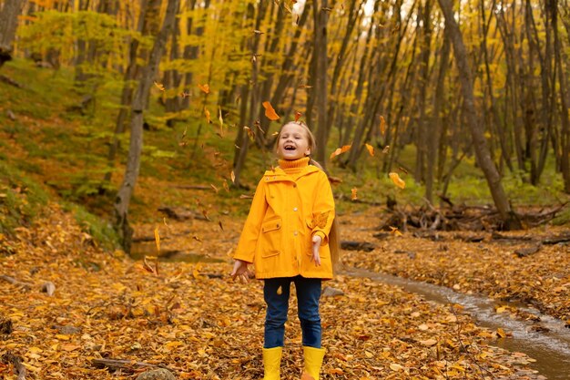 a beautiful little girl in a yellow jacket and boots walks through the urban autumn forest