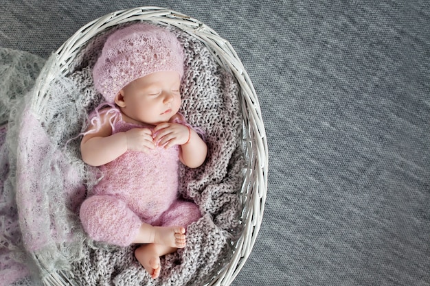 Красивая маленькая новорожденная девочка 1 месяц спит в плетеной корзине. Копировать пространство