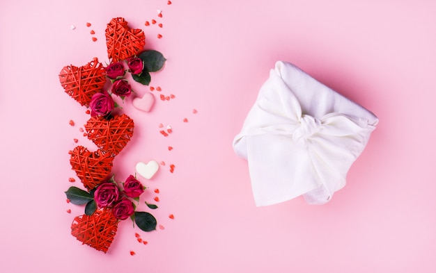 美しい小さなバラ、小さなハート、ミルクチョコレートの心、ピンク色の背景に白い色のフォロシクの美しい贈り物。