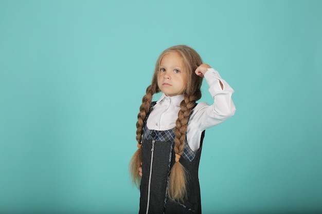 a beautiful little smiling blonde girl in a white shirt and a gray sundress is a schoolgirl