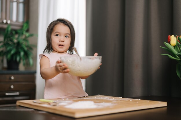 La bella bambina di due anni che indossa un abito bianco tiene per mano una ciotola trasparente