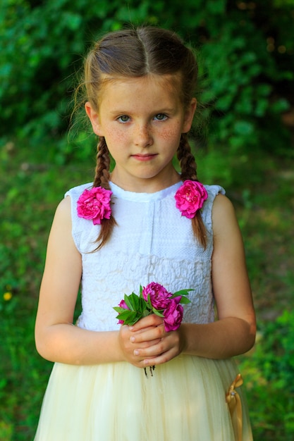 Красивый маленький молодой ребенок с цветами в руках в парке летом.