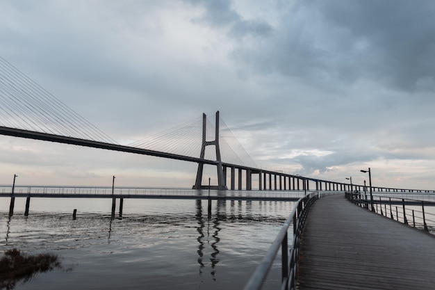 Beautiful long bridge with a wooden pier and the sea against a cloudy sky Vasco da Gama Bridge in Lisbon