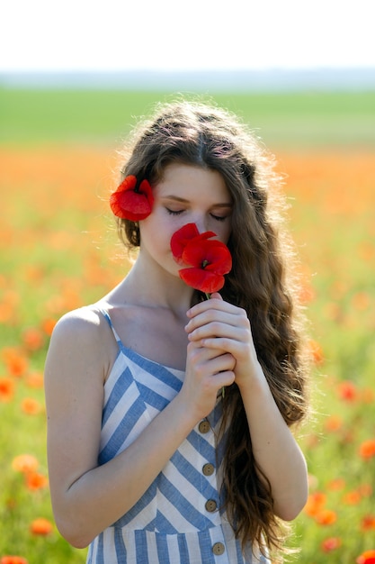 a beautiful long darkhaired girl stands with red poppies in her hands sniffs them and looks down