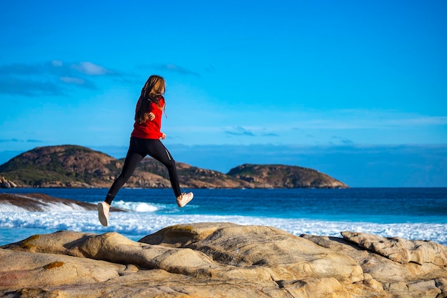 Beautiful long-haired girl jumps over rocks by the ocean girl captured while jumping in motion