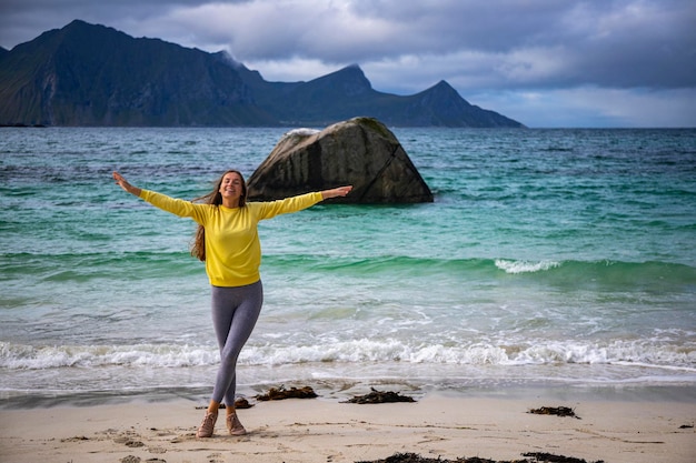 beautiful long-haired girl raises hands in the air on the famous paradise beach of haukland, norway