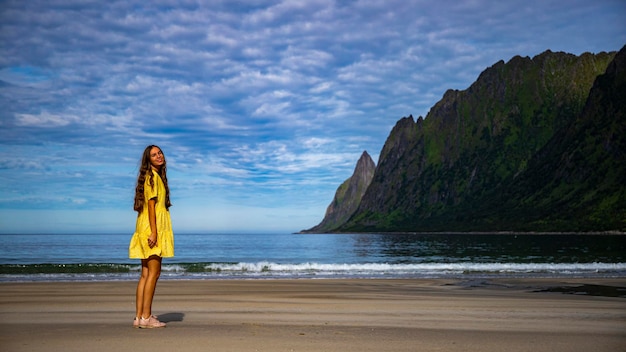 노란 드레스를 입은 아름다운 장발 소녀가 노르웨이 센야의 유명한 해변인 에르피오르드스트란다를 산책합니다.