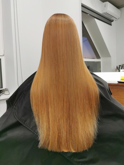 Beautiful long redhead hair girl in a beauty salon after hair care View from the back Hairdresser