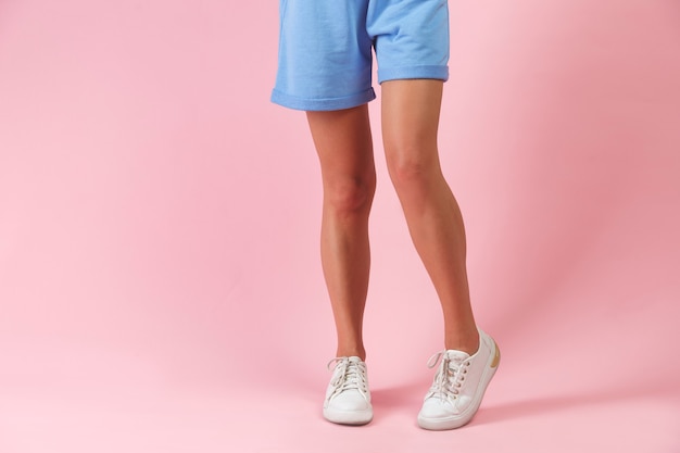 Beautiful long woman legs in shorts and white sneakers posing in studio fashion.