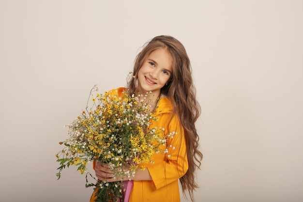 beautiful longhaired girl in a yellow raincoat with wild autumn wildflowers in her hands