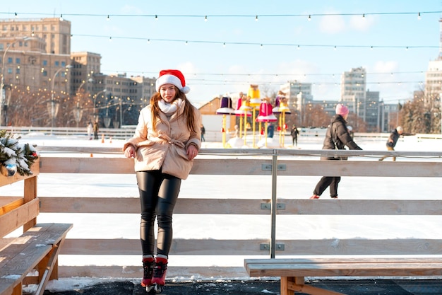 Beautiful lovely young adult woman brunet hair warm winter jackets stands near ice skate rink background Town Square Christmas mood lifestyle