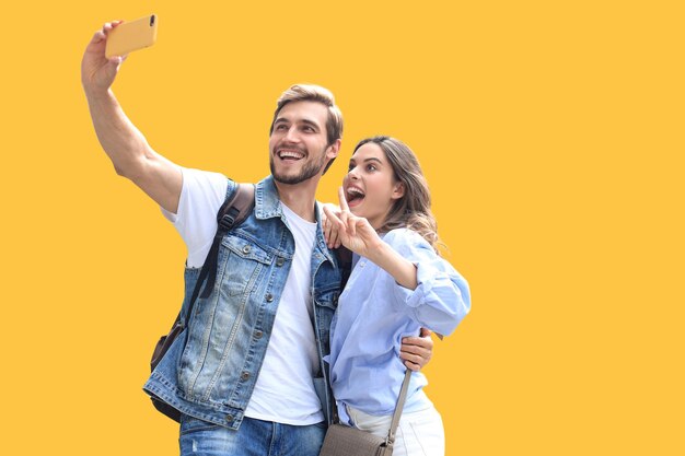 예쁜 사랑스러운 젊은 커플이 노란색 배경에 서서 셀카를 찍는 동안 포옹하고 있습니다.
