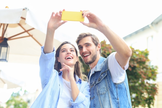 Bella giovane coppia adorabile che cammina per le strade della città, abbracciandosi mentre si fa un selfie.