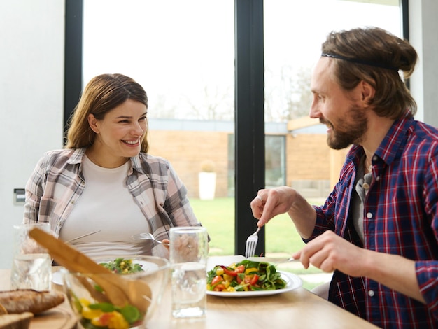 Beautiful loving young Caucasian couple sits at a table and chats cheerfully over a family dinner in a villa overlooking the garden