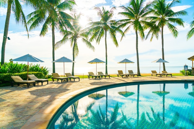 Beautiful luxury umbrella and chair around outdoor swimming pool in hotel and resort with coconut palm tree on blue sky, vacation and holiday concept