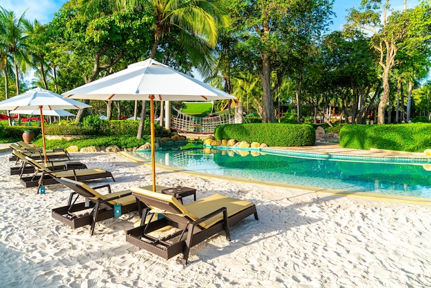 Beautiful luxury umbrella and chair around outdoor swimming pool in hotel and resort with coconut palm tree on sunset  or sunrise sky - holiday and vacation concept