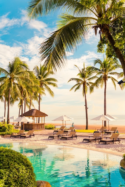 Beautiful luxury umbrella and chair around outdoor swimming\
pool in hotel and resort with coconut palm tree on sunset or\
sunrise sky - holiday and vacation concept