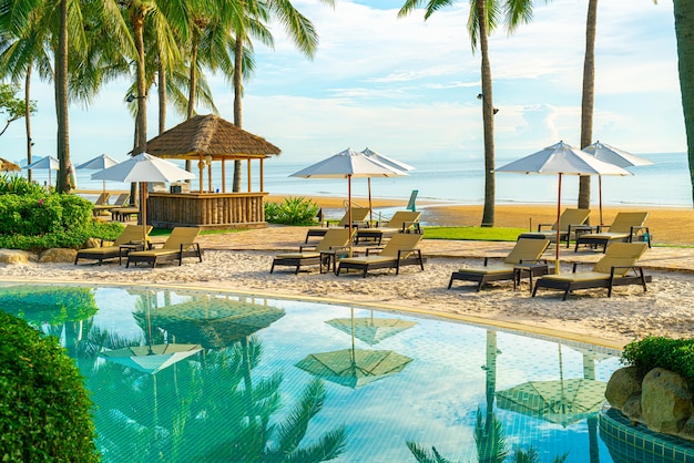 夕日や日の出の空にココナッツ椰子の木とホテルやリゾートの屋外スイミングプールの周りの美しい豪華な傘と椅子。休日と休暇の概念