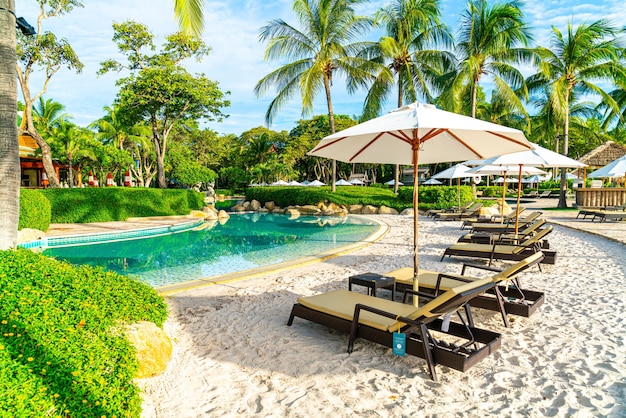 Beautiful luxury umbrella and chair around outdoor swimming\
pool in hotel and resort with coconut palm tree on sunset or\
sunrise sky - holiday and vacation concept