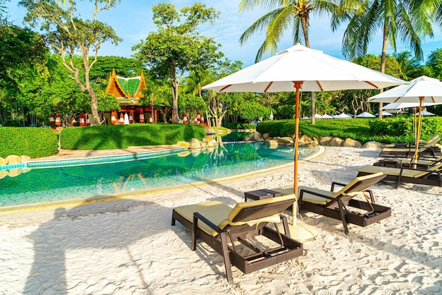 Beautiful luxury umbrella and chair around outdoor swimming pool in hotel and resort with coconut palm tree on sunset or sunrise sky holiday and vacation concept